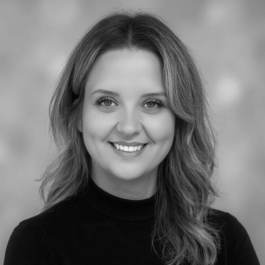 A Black and white portrait of a smiling woman with wavy shoulder-length hair, wearing a dark turtleneck.