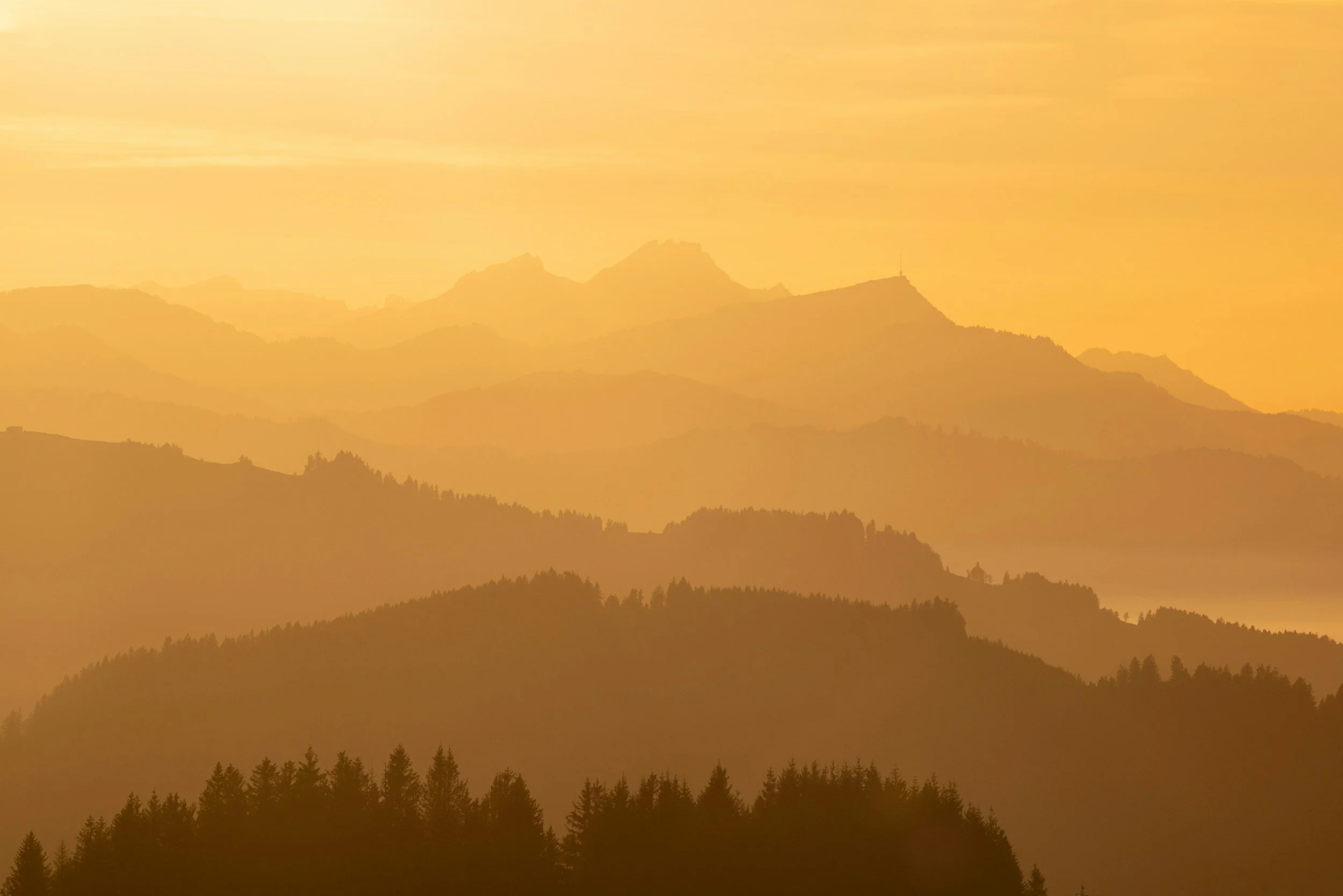 Layered mountain range during sunset with a warm golden hue.