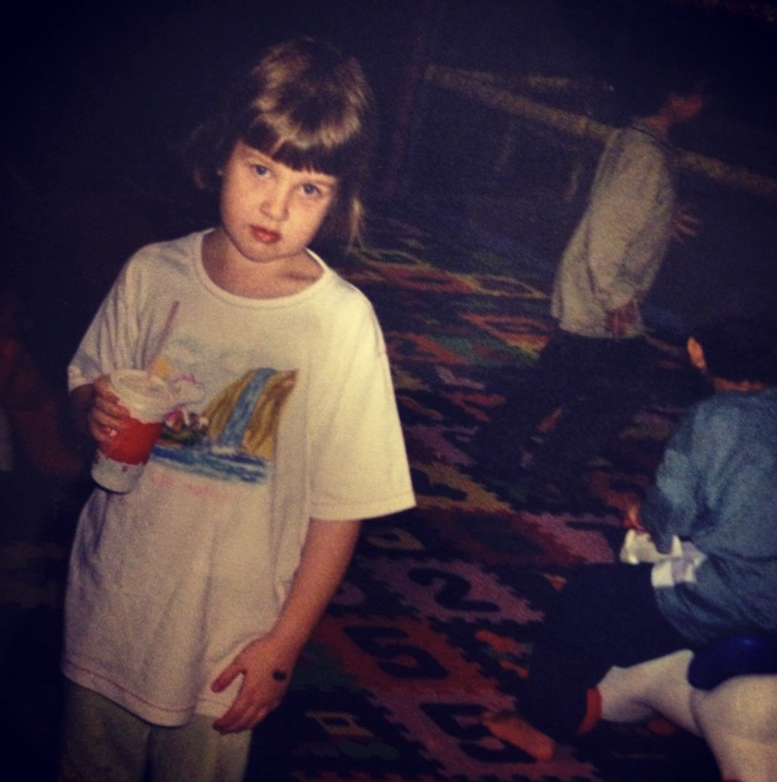 A young girl with short brown hair and freckles wearing a white t-shirt with a drawing of a castle and holding a soft serve ice cream cone.