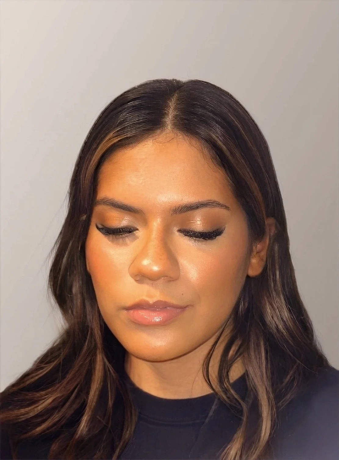 Close-up of a woman with long, wavy brown hair and makeup, with eyes closed and a neutral expression.