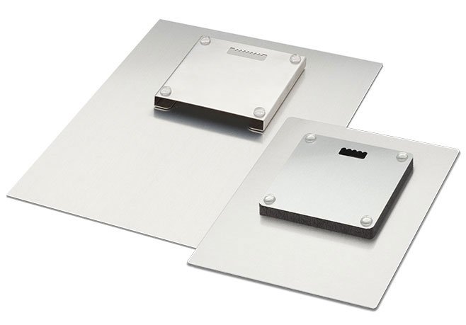 Two metal cutting blades with black foam padding are placed on top of flat metal sheets.