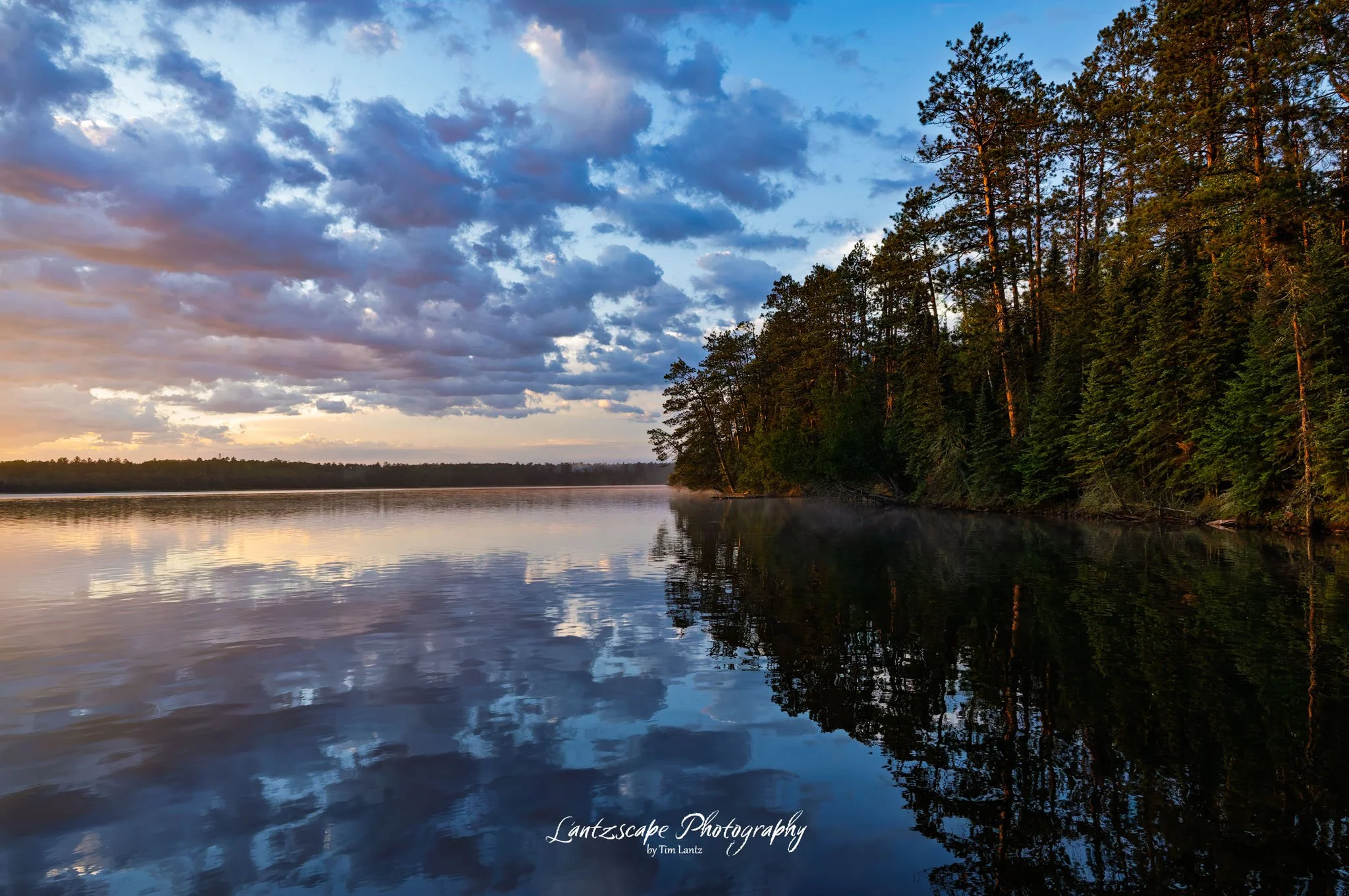 Reflection of trees and cloudy sky on a calm lake at sunset.