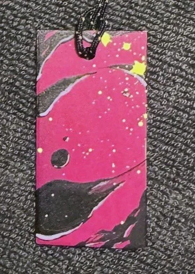 A colorful paper gift tag with black strings at the top, featuring an abstract bird design on a pink background with yellow and white splatters.