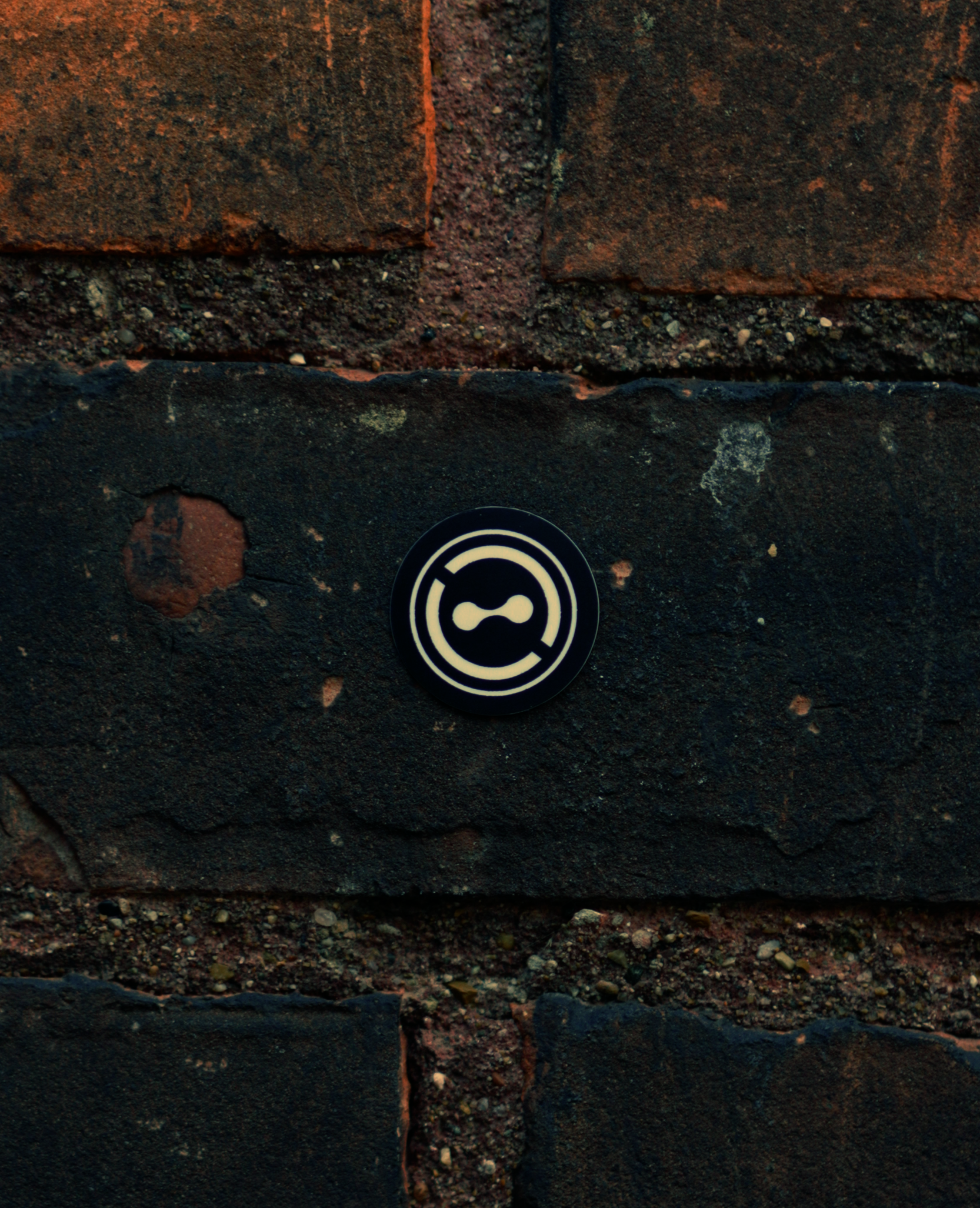 Close-up of a black and white circular security camera sticker on a dark brick wall.
