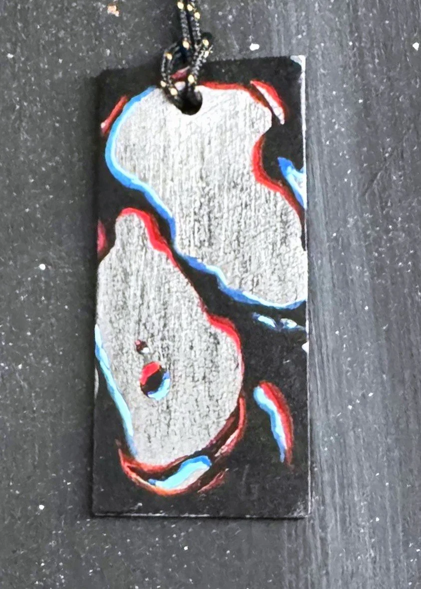 A wooden keychain with a painted outline of a dog, featuring black, red, and blue colors, hanging from a black and white string.