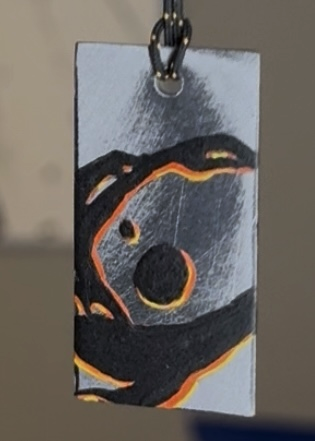 A small metallic tag with orange and black markings hanging from a chain.