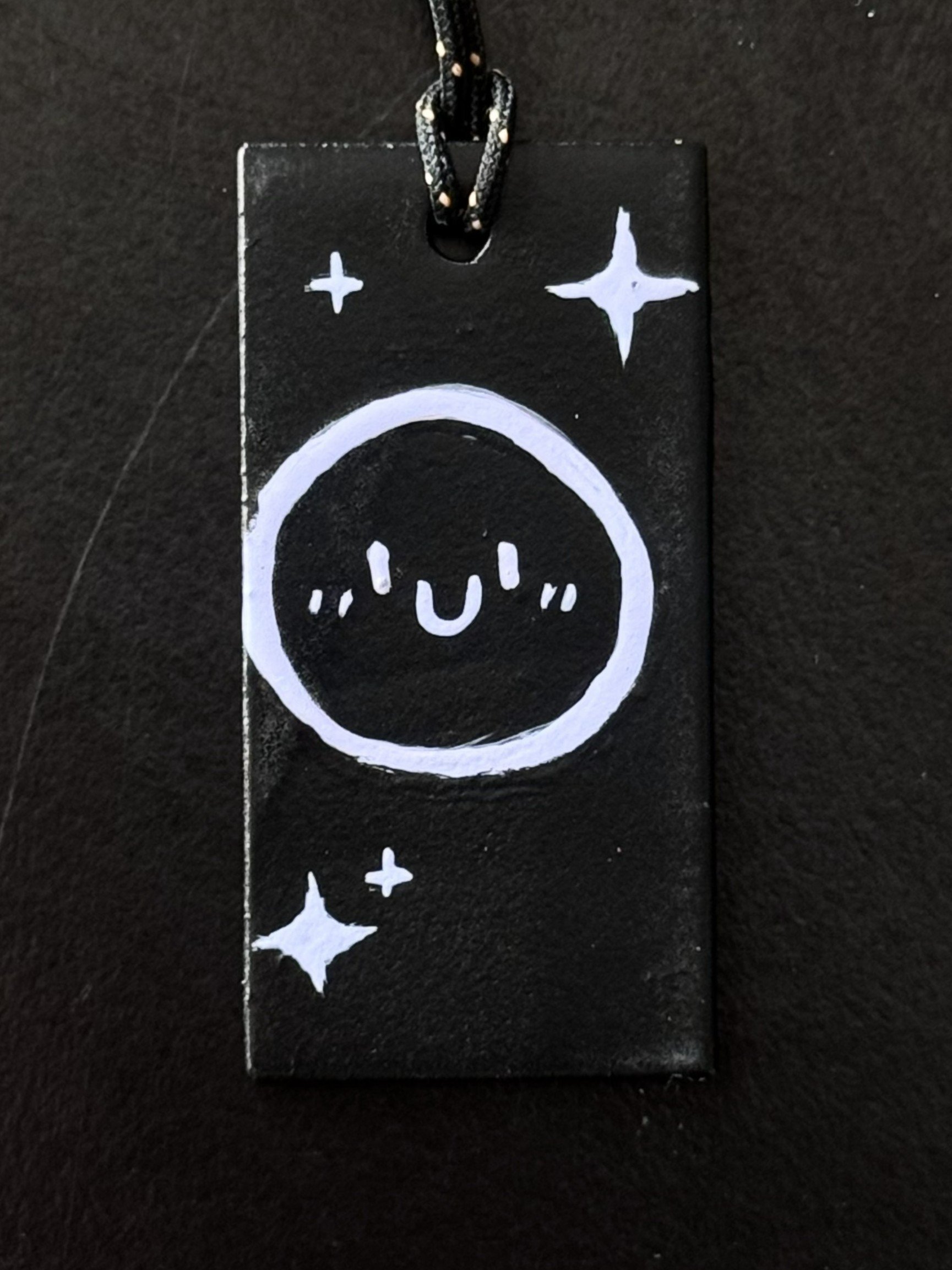 Black tag with white cartoon face and starry sparkles.
