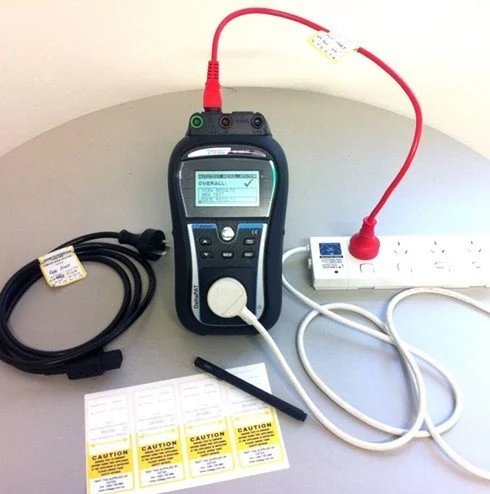 Electrical testing device connected to a power strip with caution labels nearby.