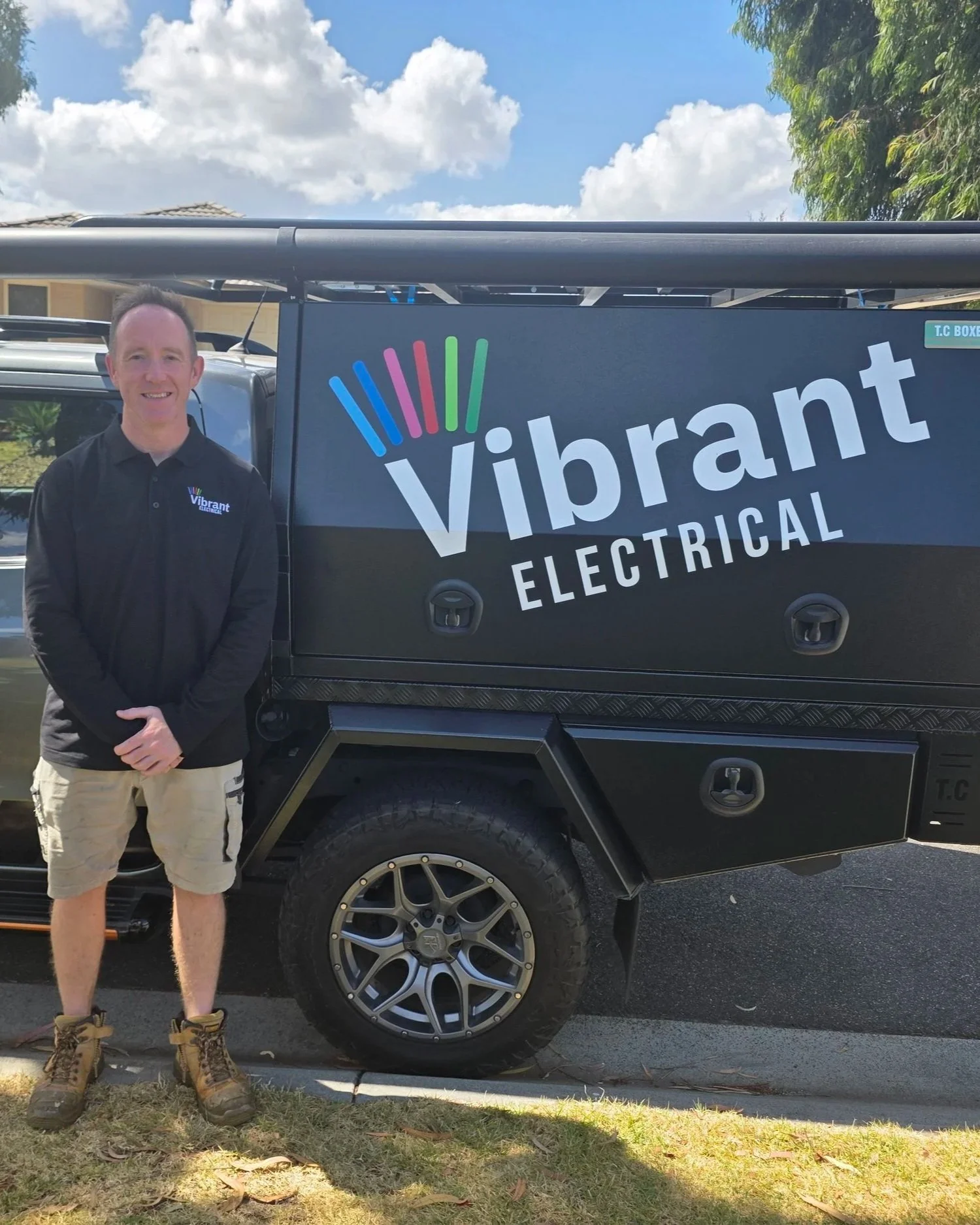 Scott standing in front of a van with the company name Vibrant Electrical on it, smiling.