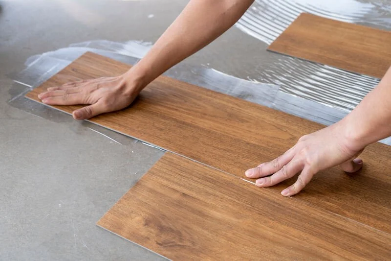 Person installing laminate flooring, pressing a wooden floorboard with hands while water is underneath.