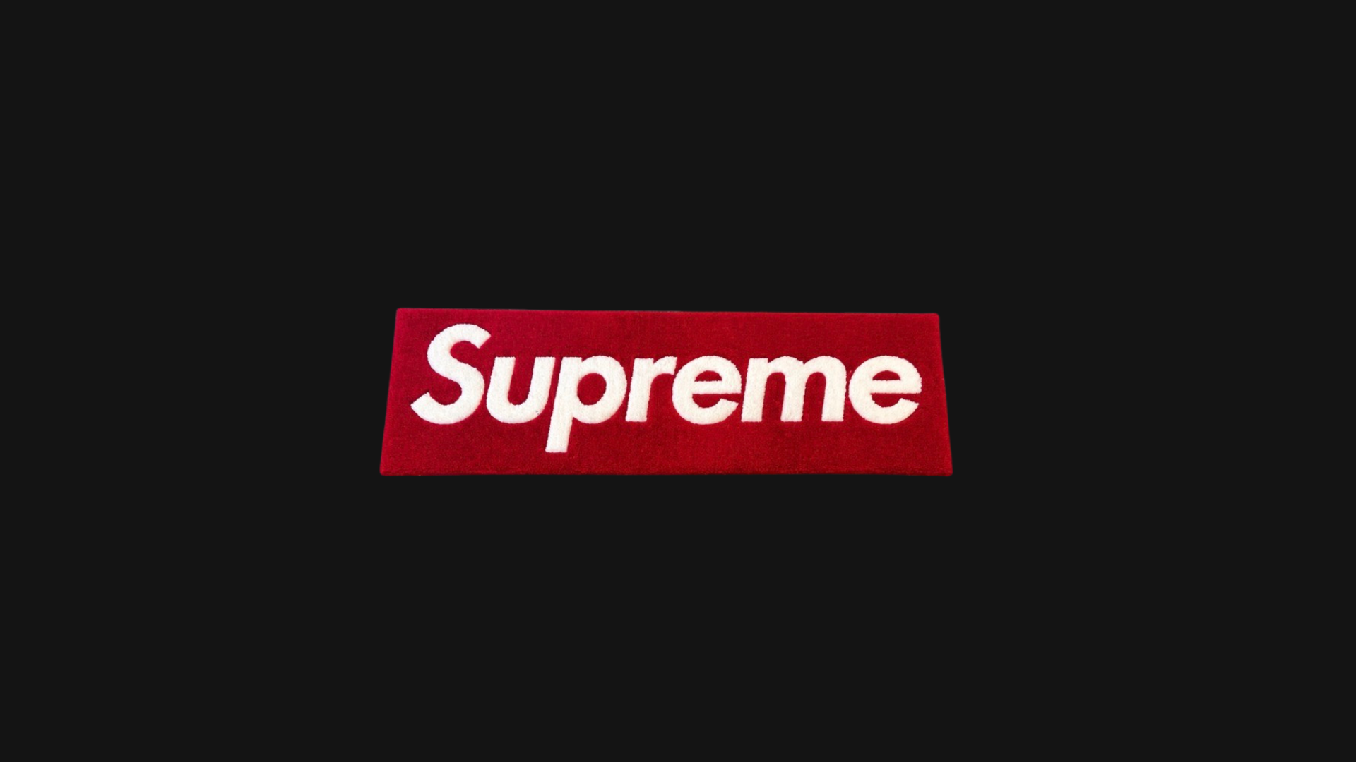 Red rectangular rug with the word 'Supreme' in white letters, placed on a black background.