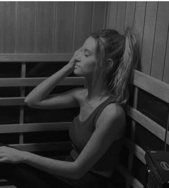 A woman sitting with her eyes closed, resting her head on her hand against a wooden wall.