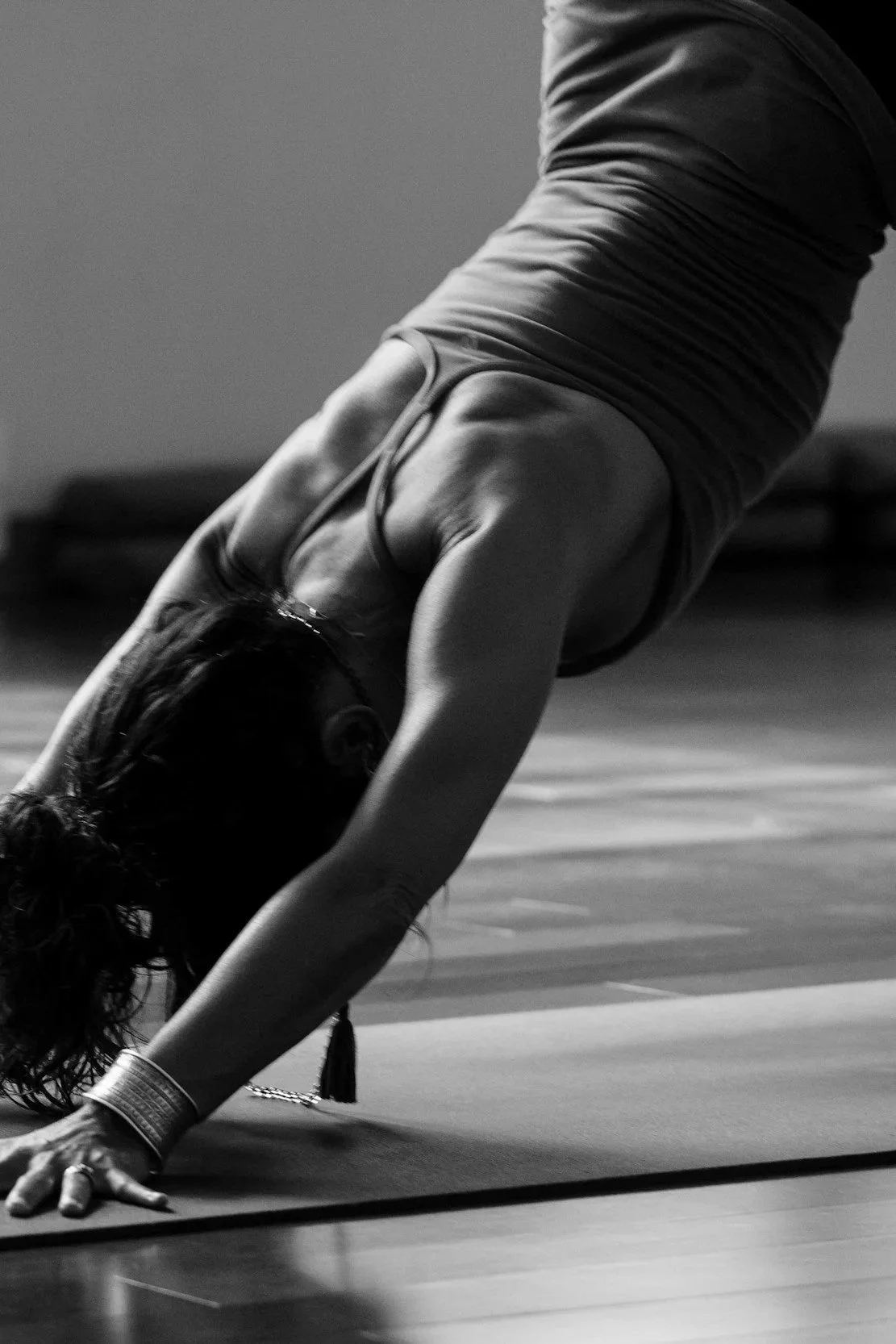 A woman practicing yoga in downward dog pose on a mat, in a dimly lit room.