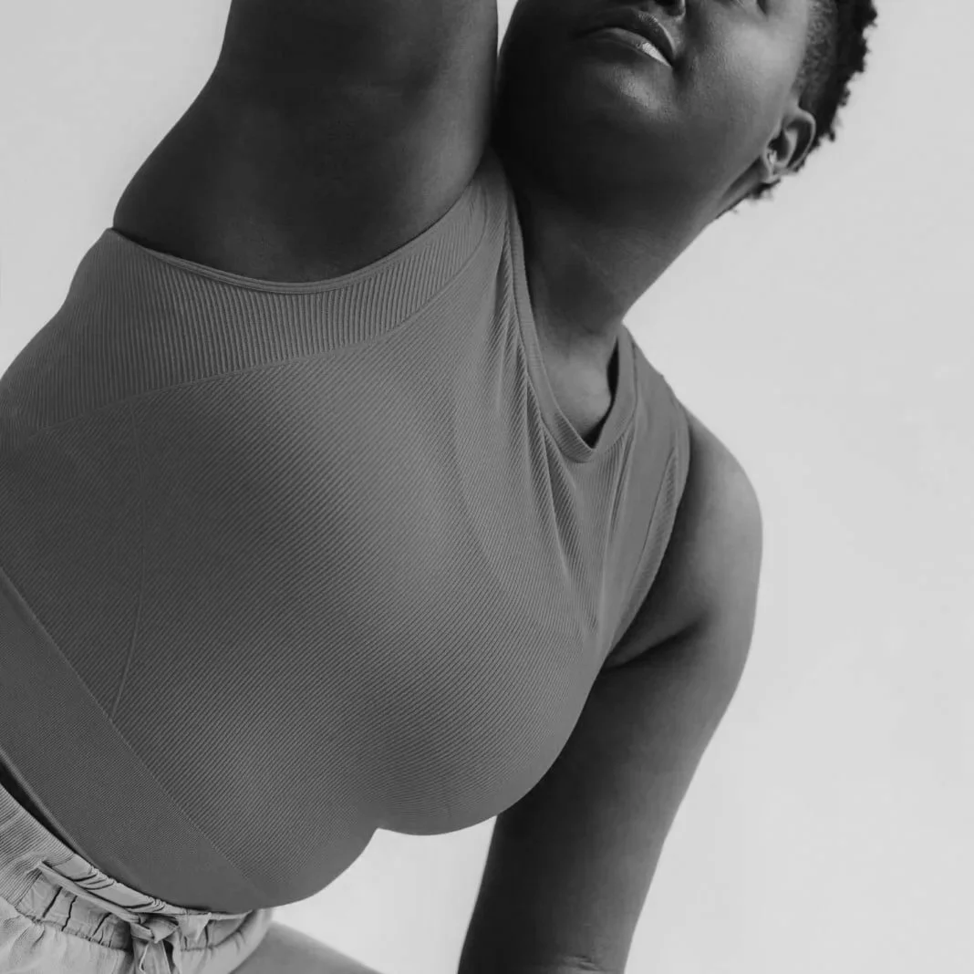 Close-up black and white photo of a woman stretching her arm over her head, wearing a fitted athletic top and shorts.