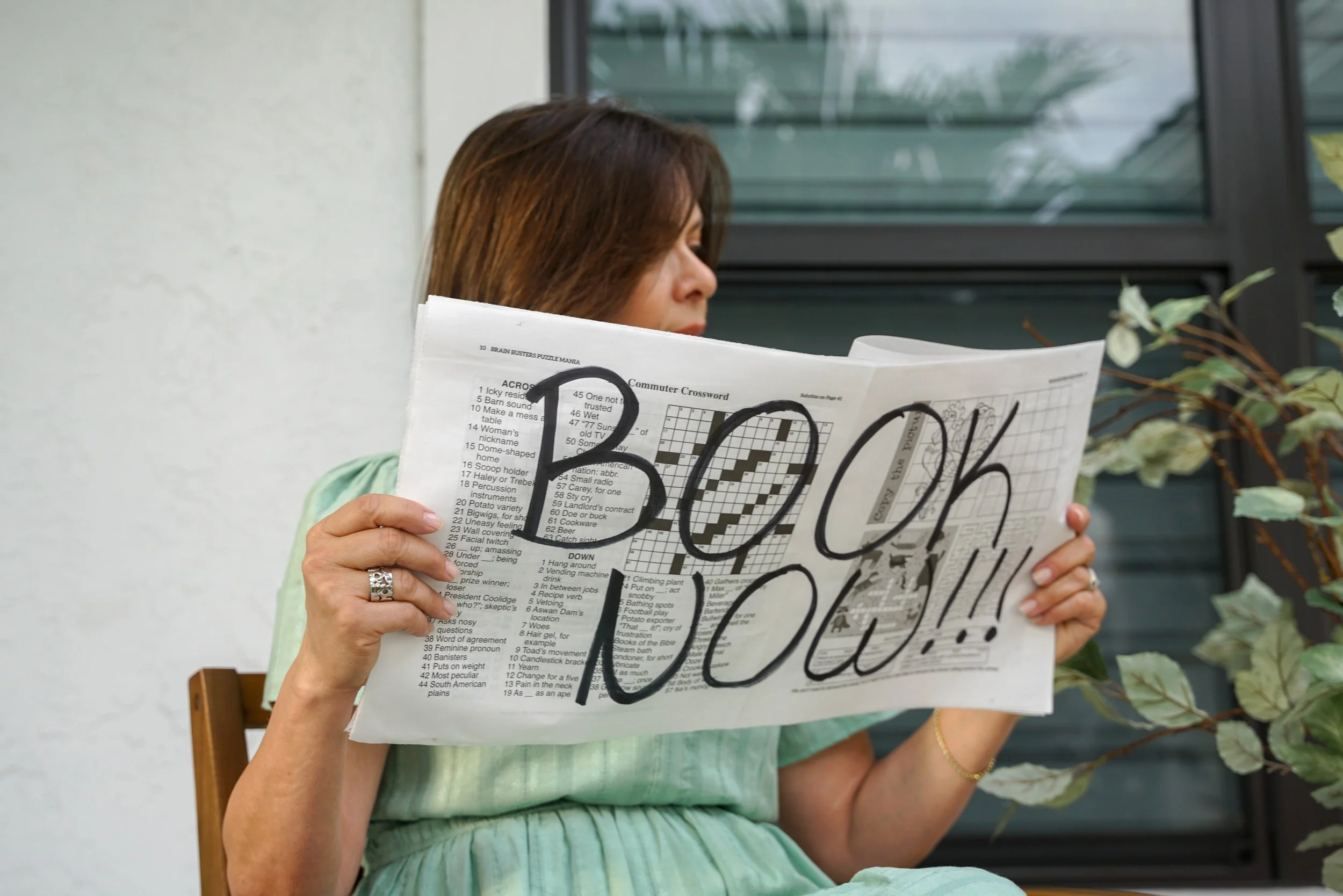 A woman holding a newspaper with large handwritten text saying 'LOOK OUT!!'.