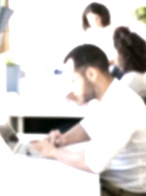 Três pessoas sentadas ao redor de uma mesa de trabalhos, usando computadores, em ambiente de escritório.