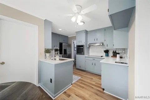 Modern kitchen with light blue cabinets, white countertops, stainless steel appliances, and hardwood floors.
