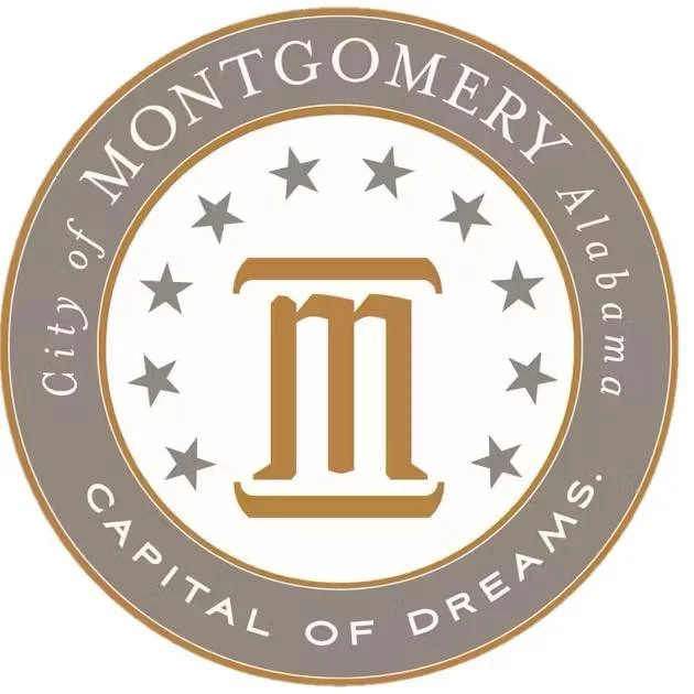 Seal or emblem with text indicating the City of Montgomery Alabama, capital of dreams, featuring a large gold pi symbol in the center surrounded by stars.