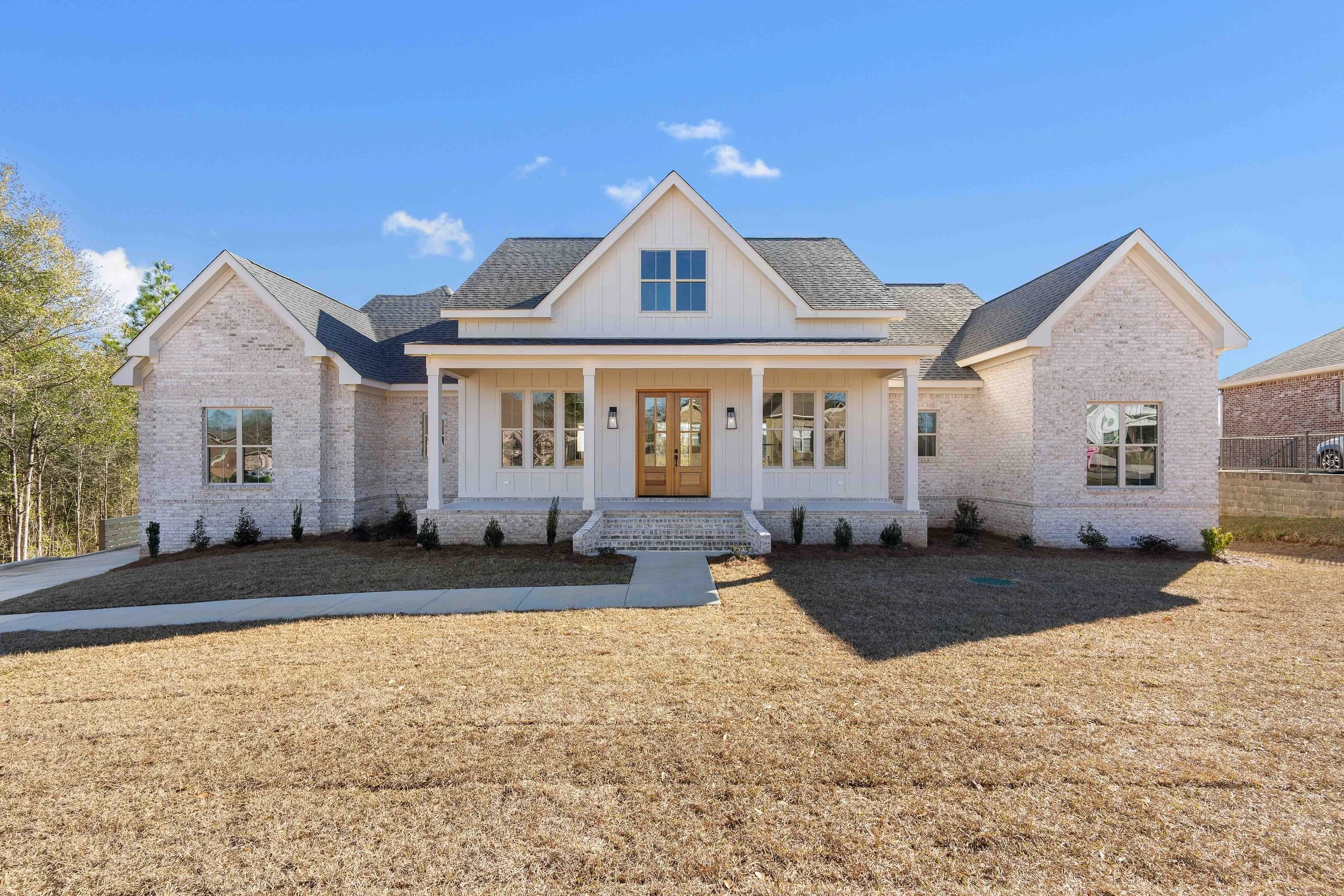 Front view of a modern house with white brick and siding, front porch, and a gabled roof under a blue sky.