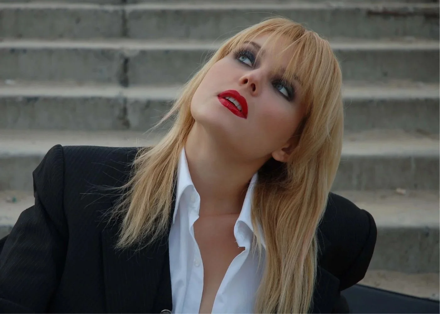 Editorial portrait of a blonde woman in a black blazer with bold red lipstick