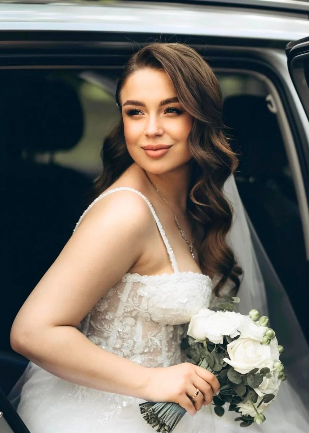 Bride by a car window with polished wedding makeup and glossy waves