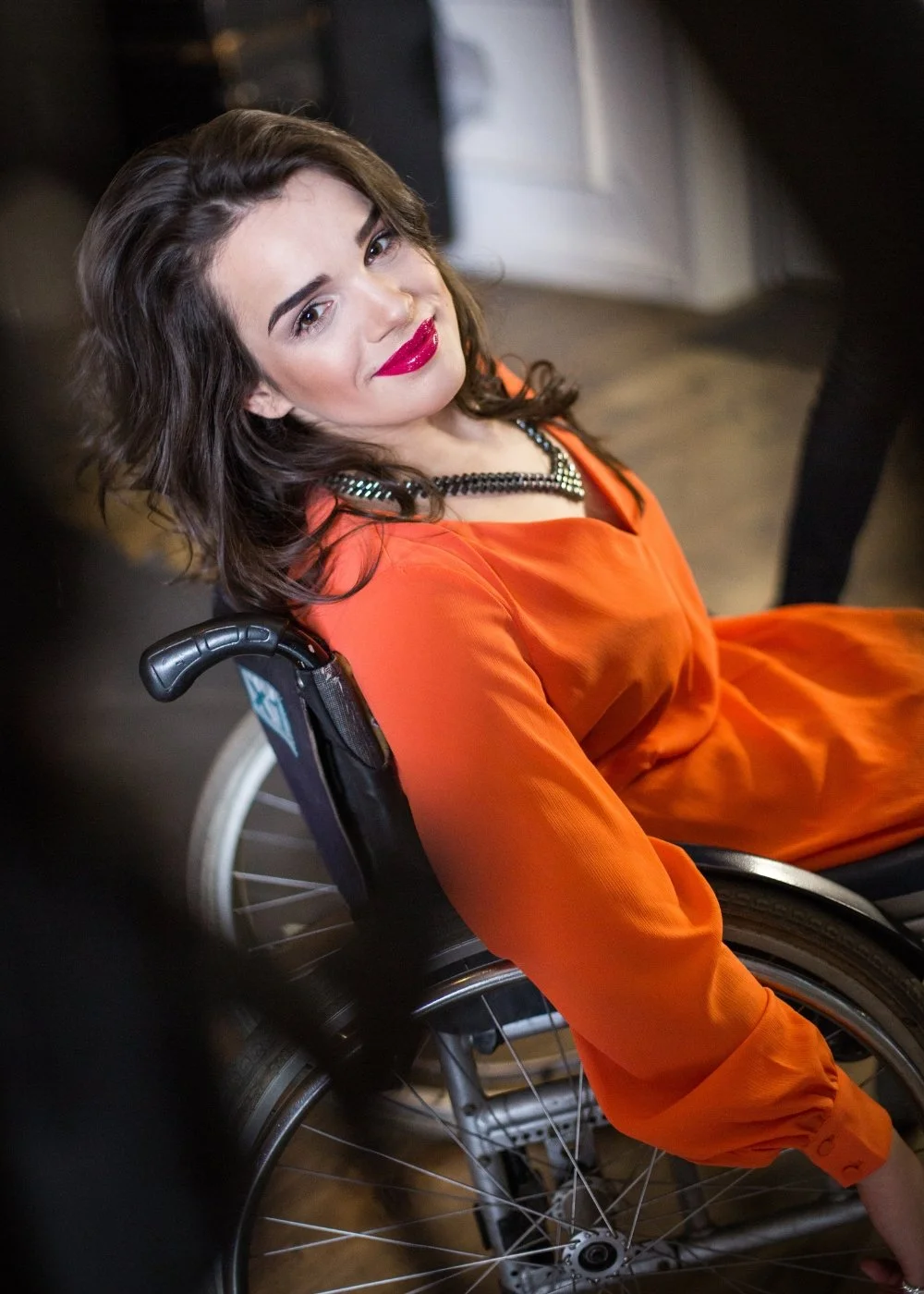 Fashion portrait of a woman in a wheelchair in an orange dress with bold lipstick (editorial look)