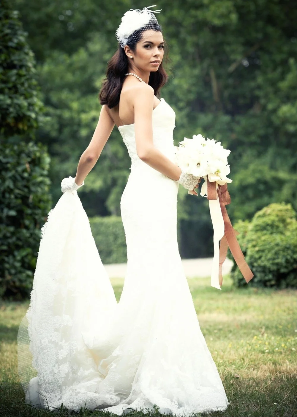 Outdoor bride in a white gown holding a bouquet, full-length wedding portrait.