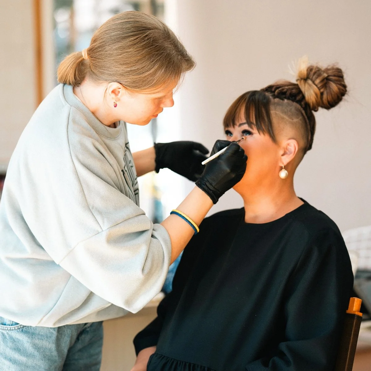 Makeup artist applying lipstick on a seated client for maternity photoshoot
