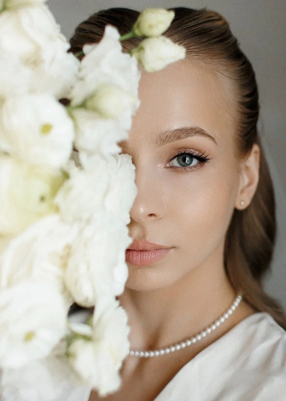 Half-face portrait behind white flowers, natural glow and defined eyes
