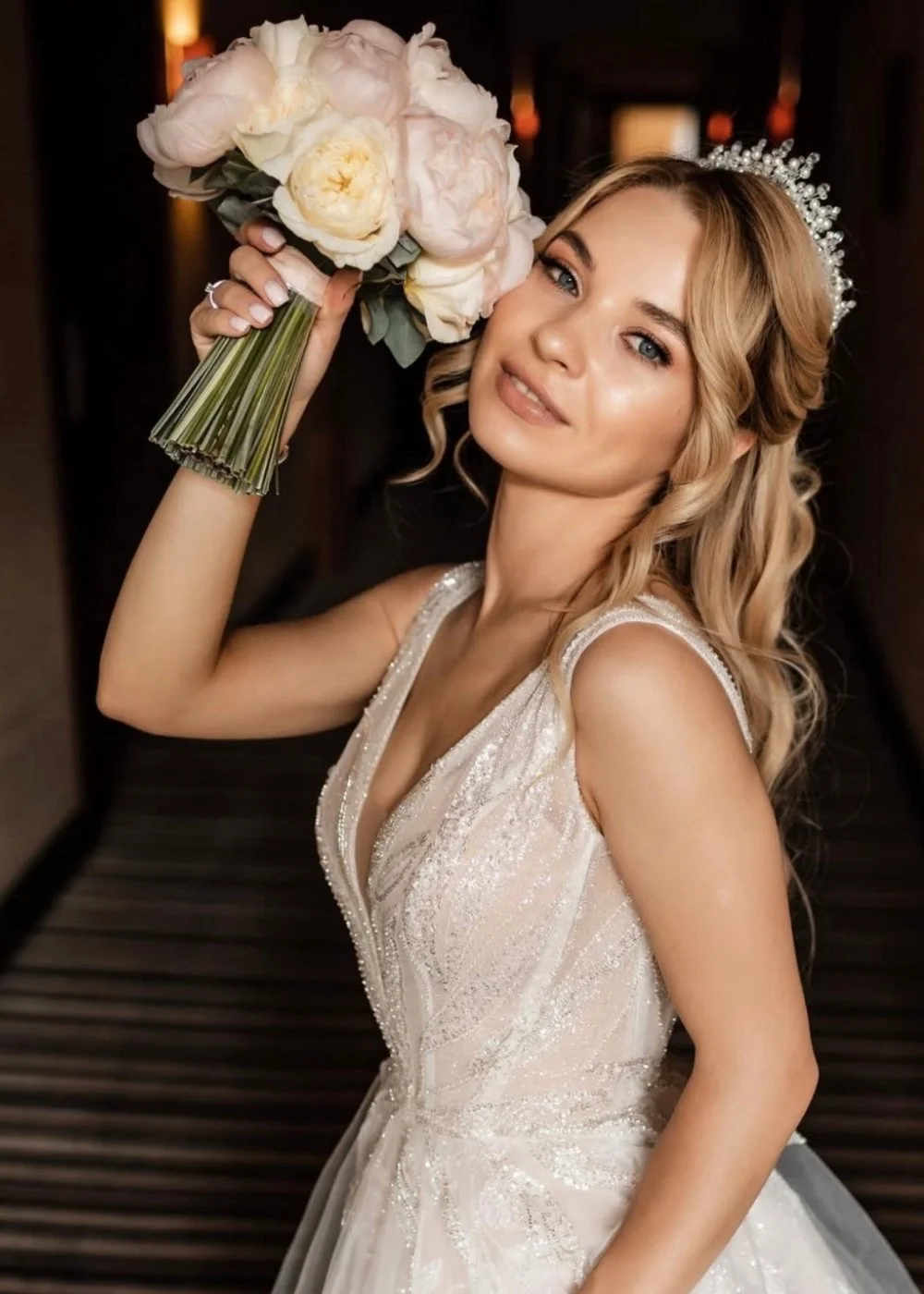 Bride holding a bouquet with soft glam wedding makeup in warm indoor light