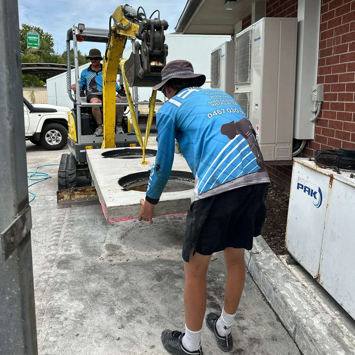 A photo of Michael driving a digger while Lachy directs a concrete slab.
