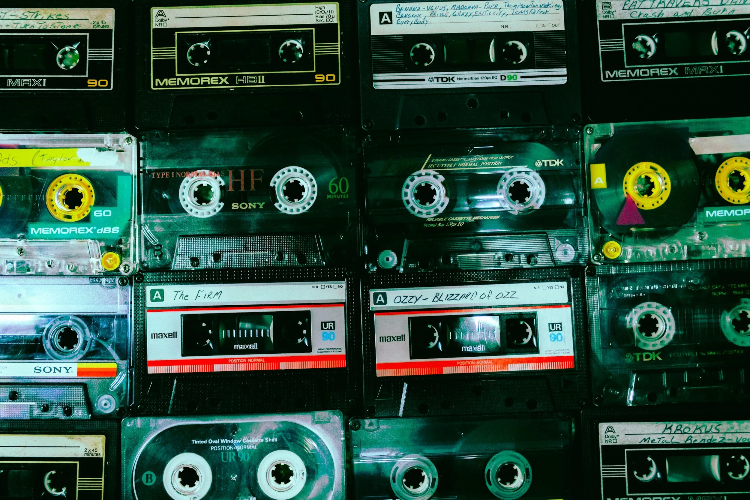 A collection of vintage audio cassette tapes, some with handwritten labels, arranged in a grid pattern.