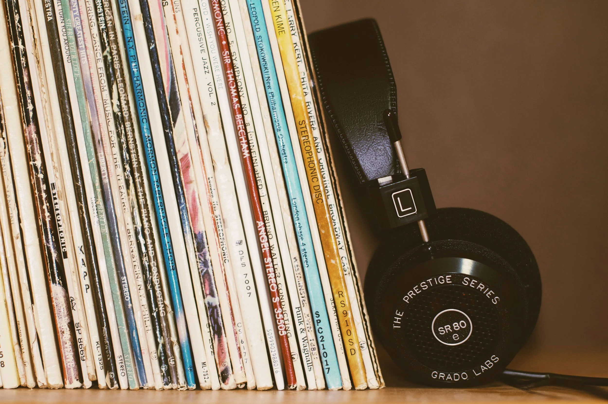 A collection of vinyl records on a shelf with a black headphone resting on top. The records have colorful and varied album covers.