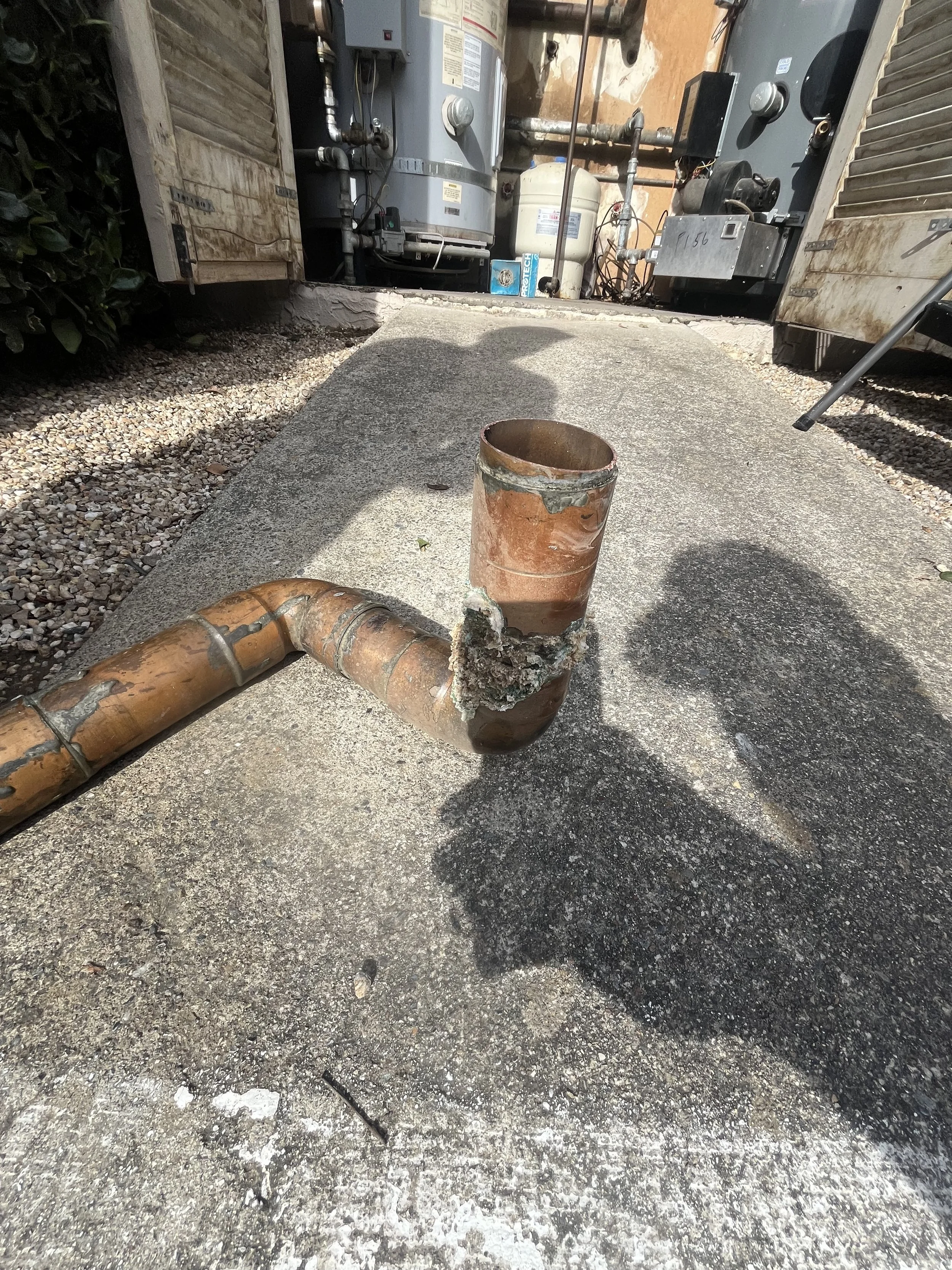 Corroded copper pipe with a broken joint on concrete ground.