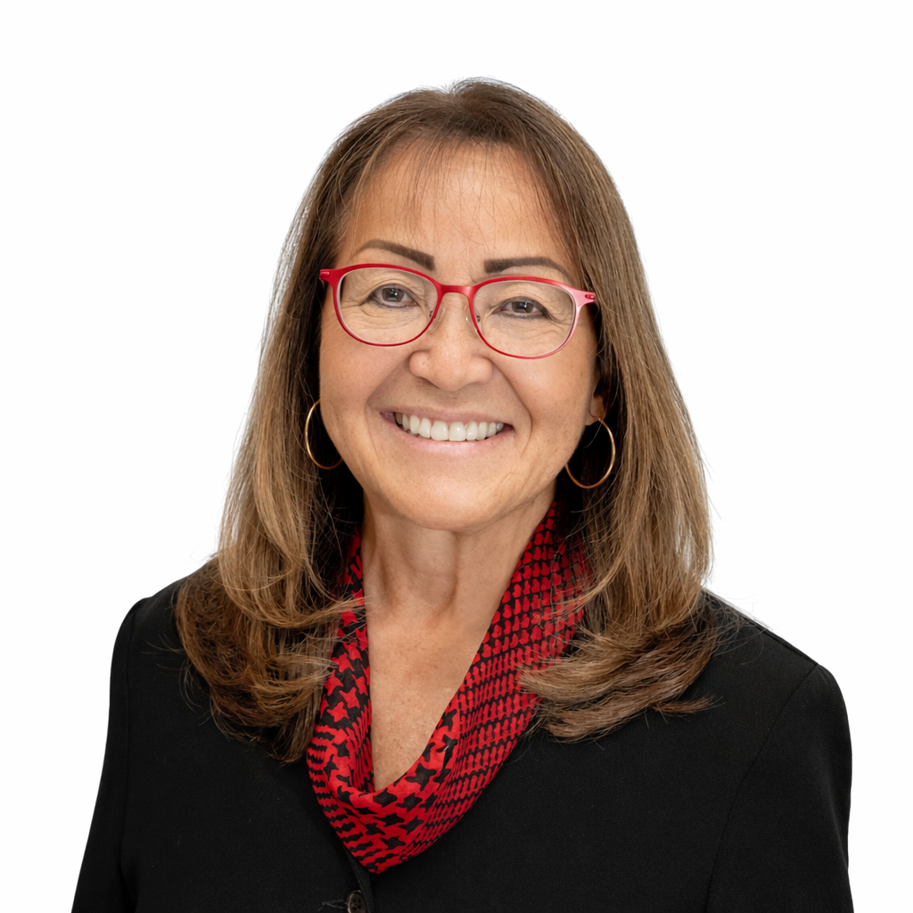 A smiling middle-aged woman with shoulder-length brown hair, wearing red glasses, hoop earrings, a black blazer, and a red and black patterned scarf against a white background.