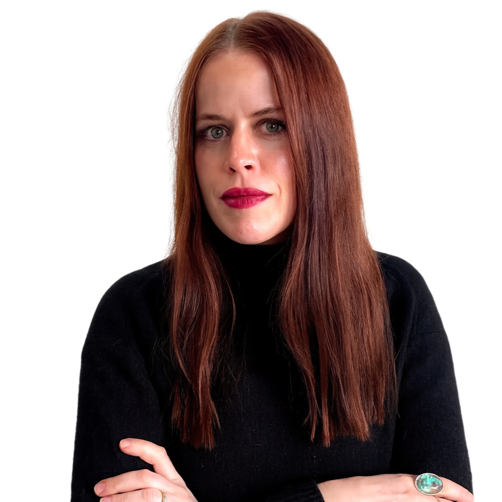 A woman with long red hair wearing a black turtleneck, crossing her arms, against a white background.