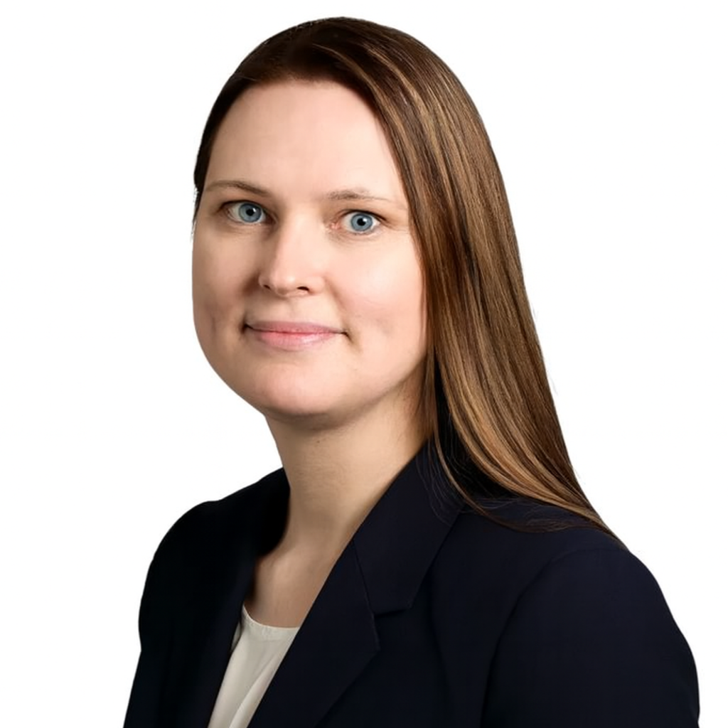 Professional woman with long red hair, blue eyes, wearing a dark blazer and light-colored top, posing against a white background.