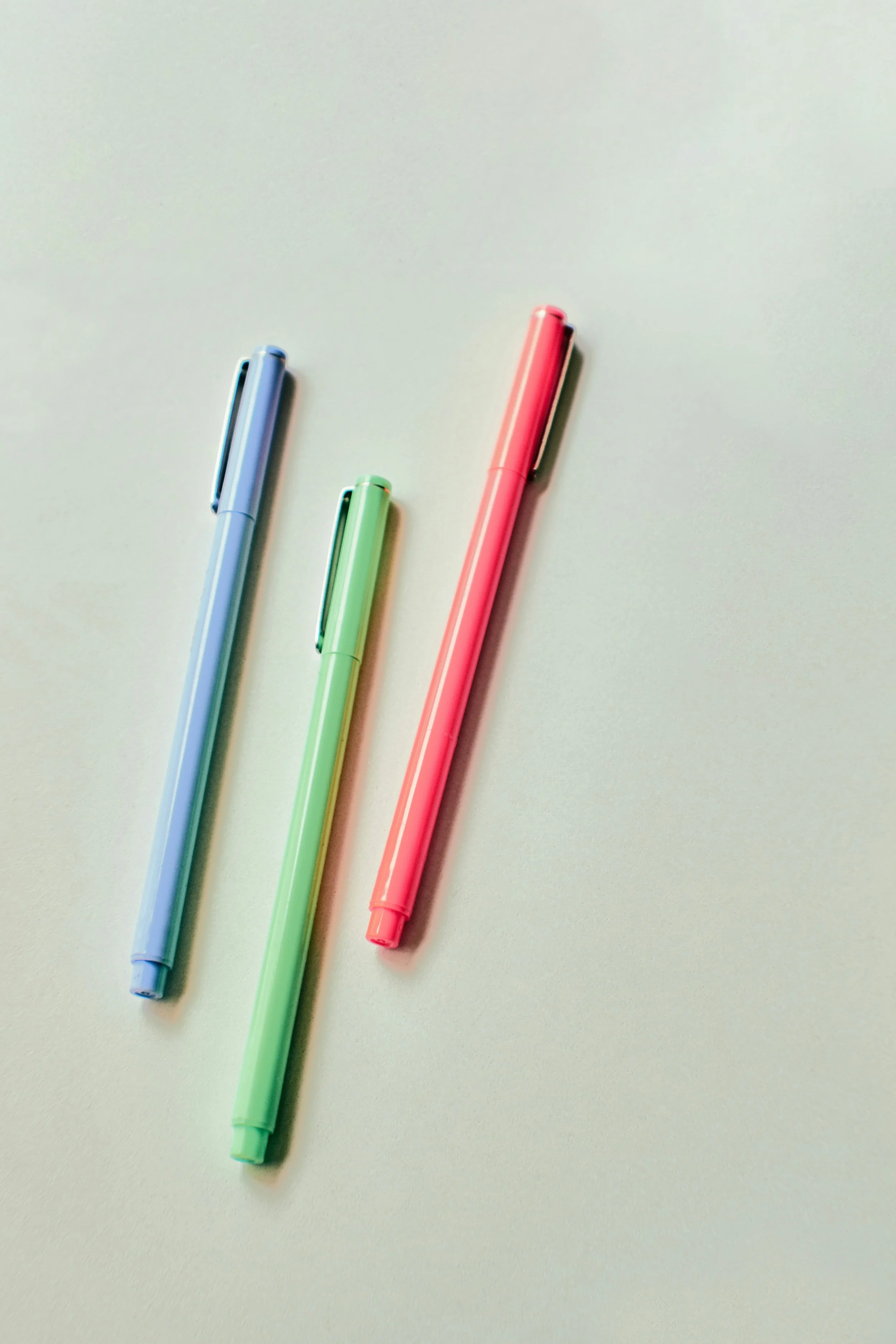 Three colorful gel pens in blue, green, and pink lying on a white surface.