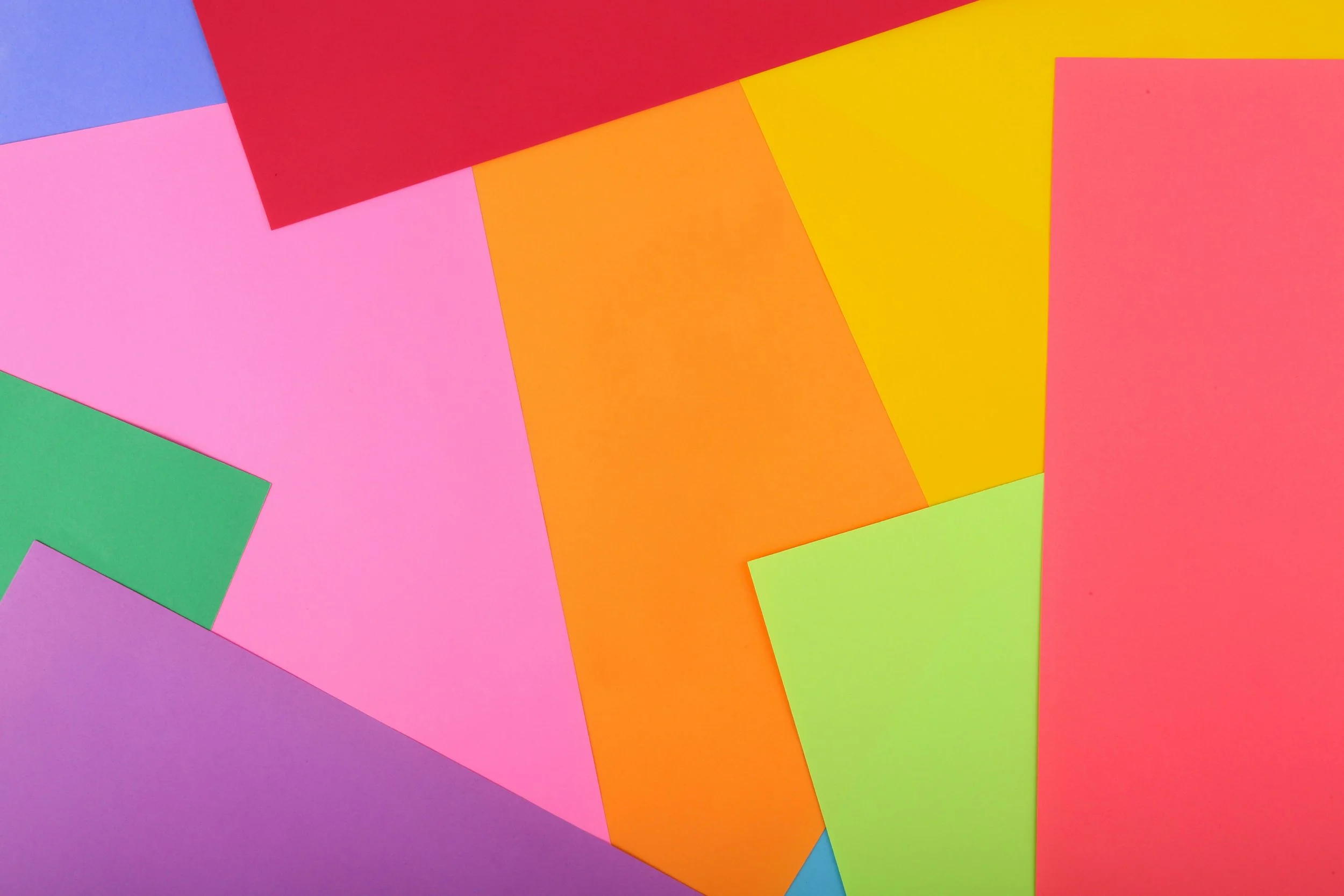 Colorful sheets of paper in various colors including pink, green, purple, orange, yellow, red, and blue, arranged overlapping on a flat surface.