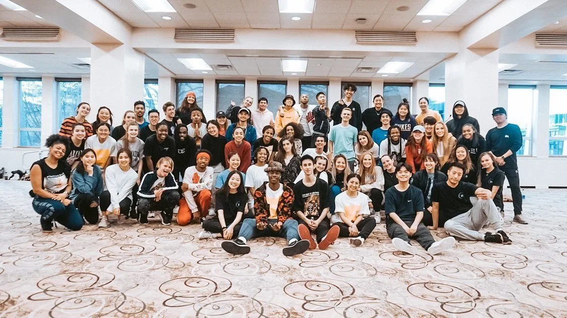 Group of diverse young people posing in a large, well-lit room with large windows.