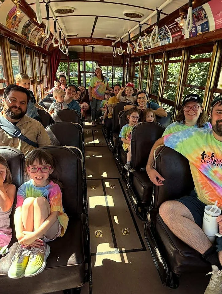 A group of people, including children and adults, sitting inside a vintage trolley bus, smiling and posing for a photo.