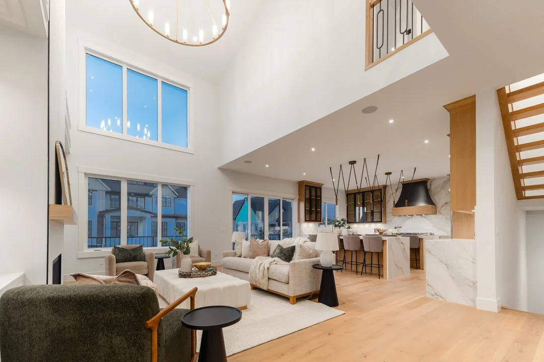 Modern living room with high ceilings, large windows, and open kitchen with bar stools.