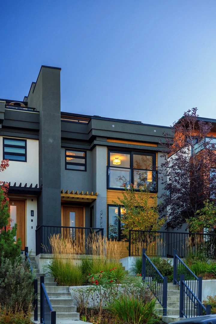 Modern multi-story residential building with large glass windows, outdoor stairways, and landscaped garden in front.