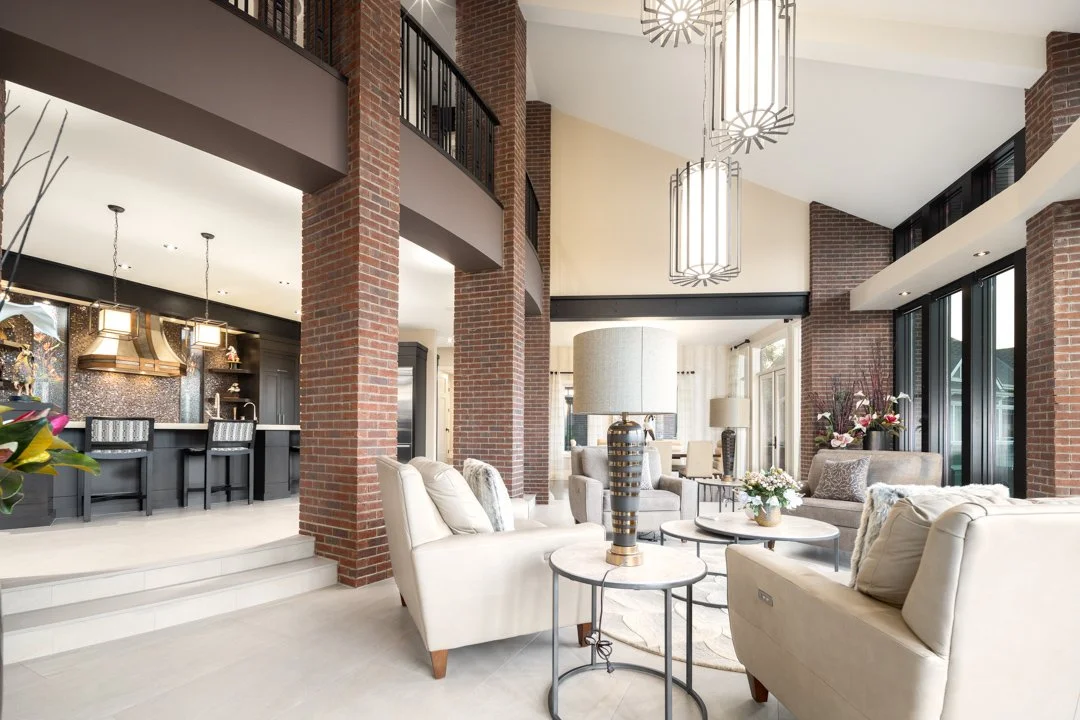 Spacious living room with modern furniture, brick walls, large windows, and hanging ceiling lights.
