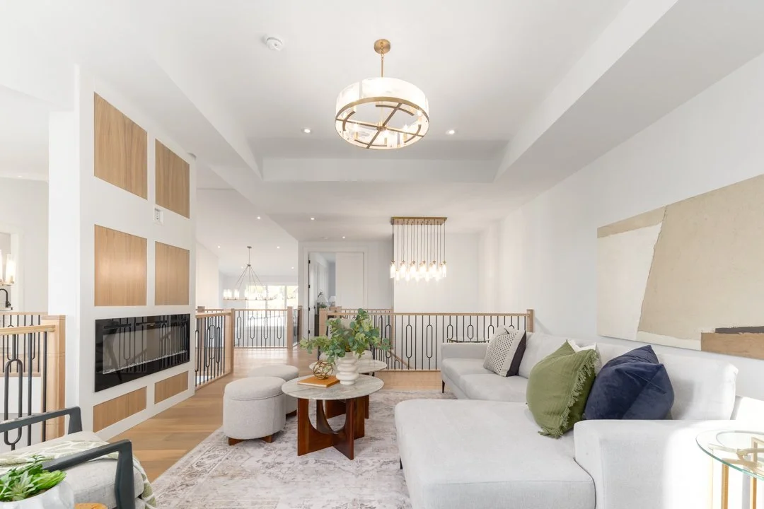 Bright living room with white walls, modern chandelier, built-in fireplace, and gray sectional sofa with green, beige, and navy pillows.