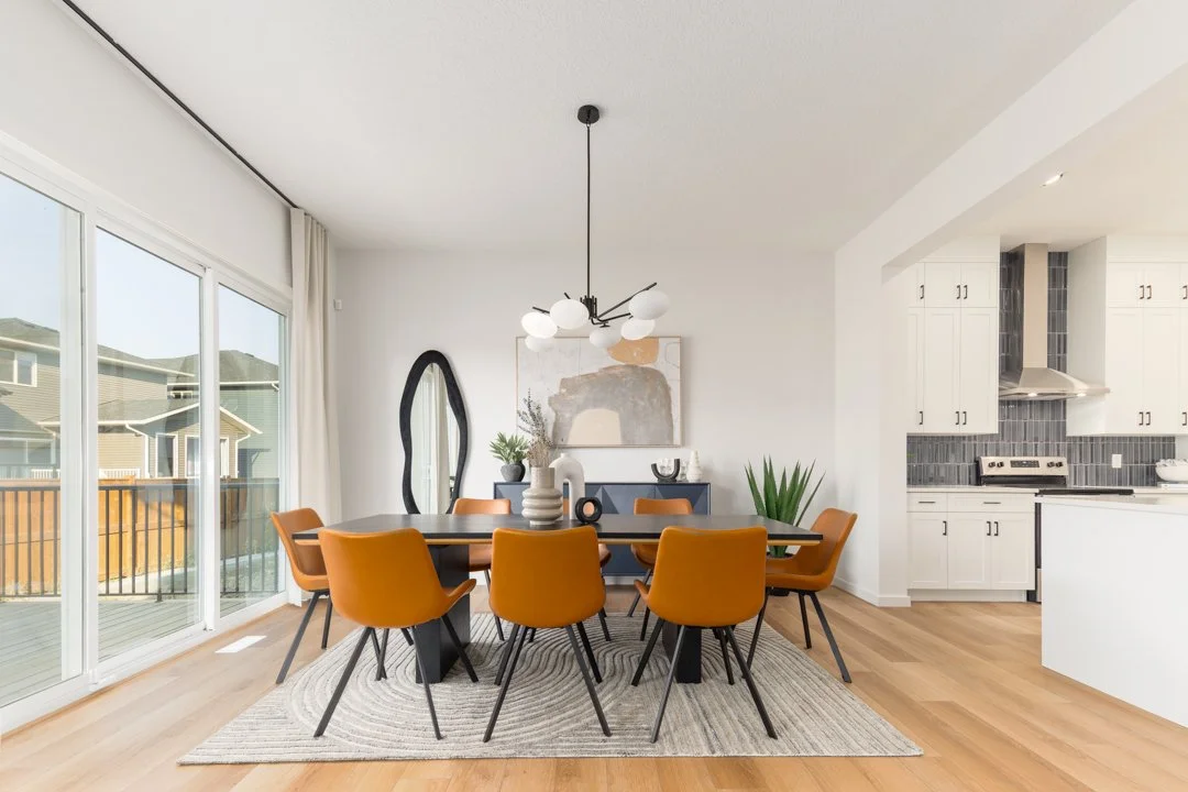Dining room with a black table, orange chairs, and modern decor, adjacent to a kitchen with white cabinets and black tile backsplash, large sliding glass doors leading to an outdoor deck.