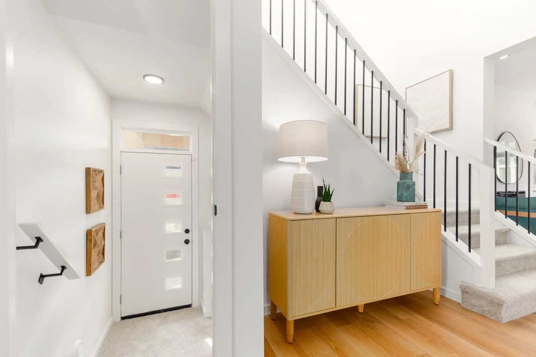 Interior view of a modern home entryway and staircase with a light-colored wooden sideboard, decorative items, and wall art.