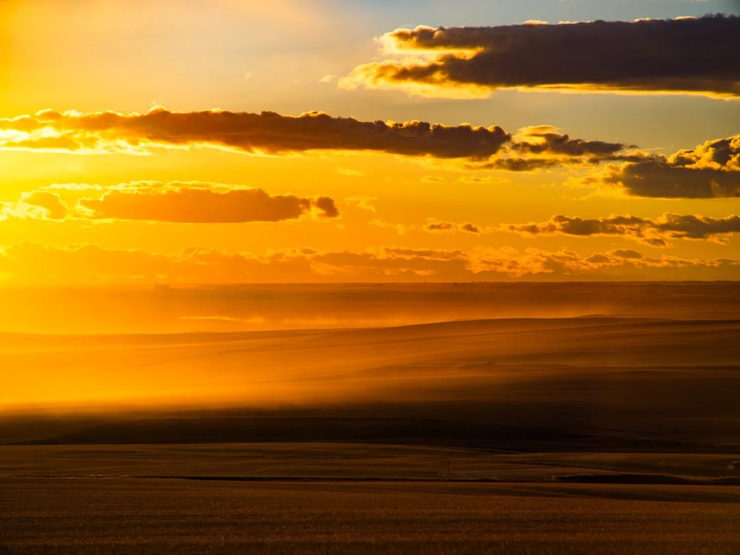 A sunset over a flat open field with clouds in the sky.