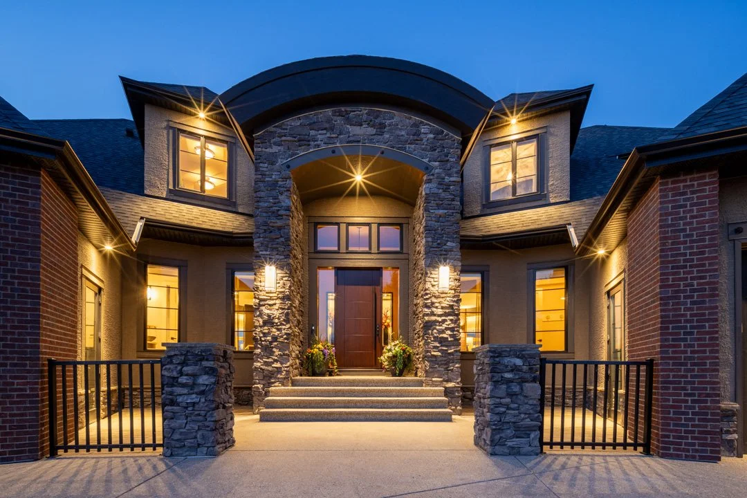 Front view of a modern house with a stone and brick facade, illuminated at dusk.