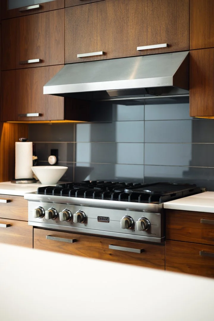 Modern kitchen with wooden cabinets, stainless steel range hood, gray tiled backsplash, and a gas stove.